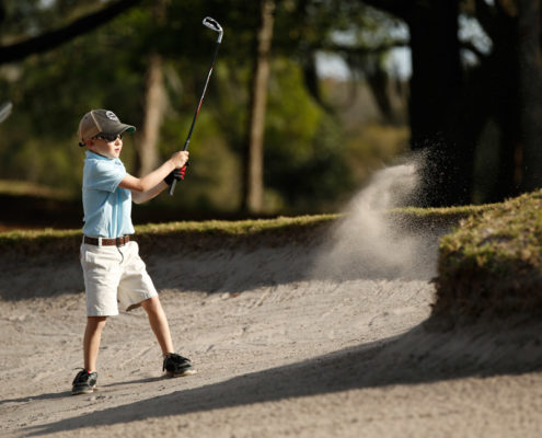 boy hitting golf ball out of sand